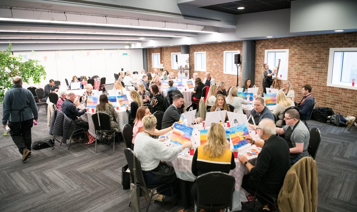 Groups sat at round tables painting on individual canvases