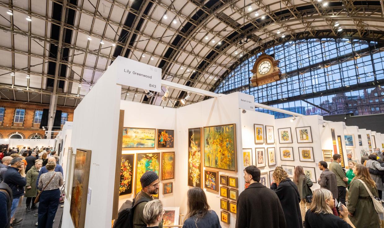 Paintings shown in booths in a busy art fair, under the large clock and arched roof of Manchester Central.