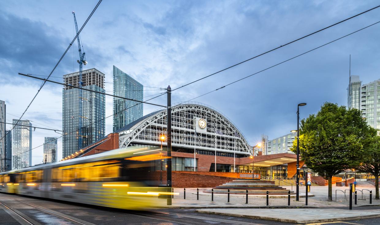 Tram passing at speed in front of Manchester Central and surrounding Manchester skyline.